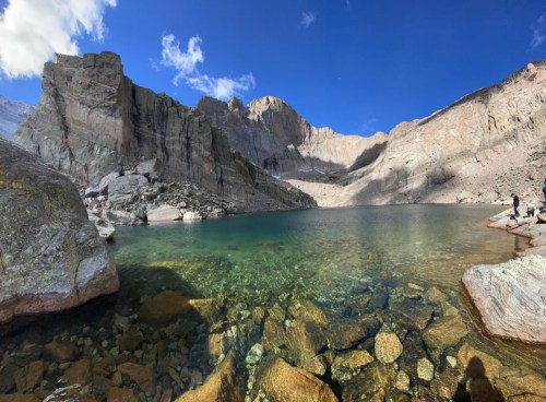 A serene mountain lake surrounded by rocky cliffs and clear blue skies, with visible rocks beneath the water's surface.