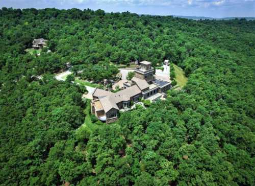 Aerial view of a large house surrounded by dense green trees and winding paths in a natural landscape.