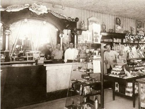 A vintage store interior with two men behind the counter and shelves filled with various products.