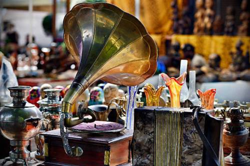 A vintage gramophone surrounded by various antique items and decorative objects in a market setting.