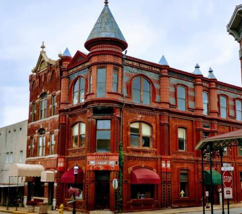 Historic red brick building with a turret, featuring large windows and decorative details, in a small town setting.