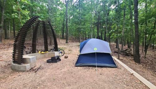 A tent set up in a wooded area next to a unique wooden structure and a bicycle.