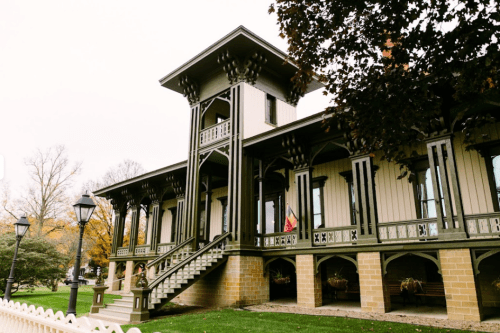 A historic building with ornate architecture, featuring a tower, balconies, and a landscaped yard.