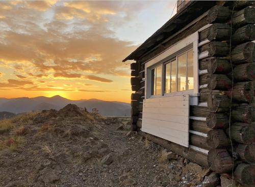 A rustic log cabin at sunset, with mountains in the background and a colorful sky.