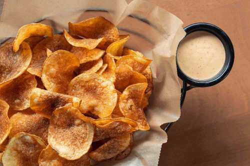 A basket of crispy potato chips next to a small bowl of creamy dipping sauce.