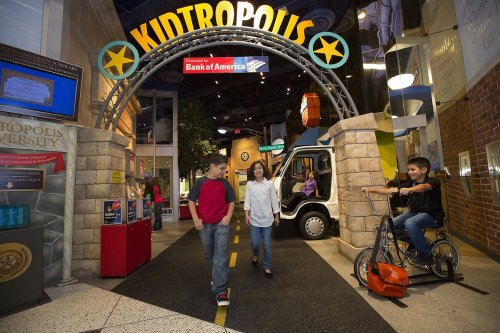 Children explore a colorful indoor play area called Kidtropolis, featuring a mock bank and various interactive activities.