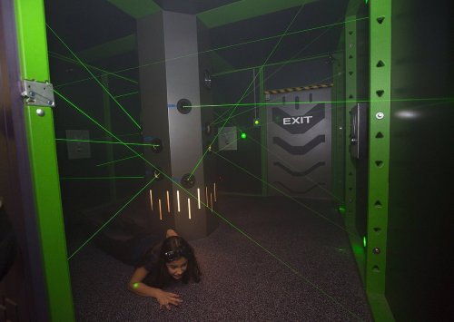 A person crawls through a room filled with green laser beams, approaching an exit door.