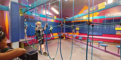 A colorful indoor climbing area with ropes and harnesses, featuring children navigating the obstacle course.