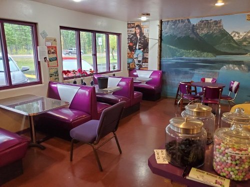 A colorful diner interior with purple booths, tables, and candy jars, featuring mountain scenery on the wall.