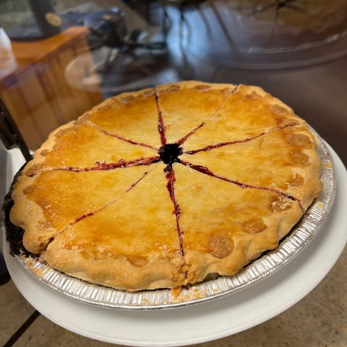 A freshly baked pie with a golden crust, sliced into eight pieces, showing a berry filling.