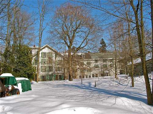 A snowy landscape featuring a large, multi-story building surrounded by bare trees and green tarps.