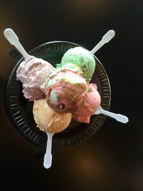 A bowl of five colorful ice cream scoops with spoons, featuring pink, green, brown, and cream flavors.
