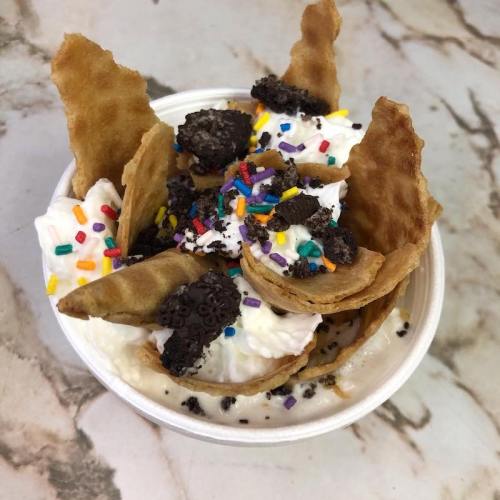 A cup of ice cream topped with whipped cream, cookie pieces, and colorful sprinkles, served in crispy waffle chips.