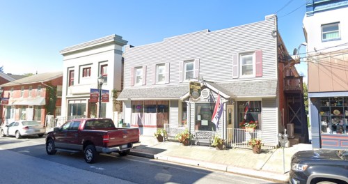A street view of a small town with a two-story building, shops, and parked cars under a clear blue sky.