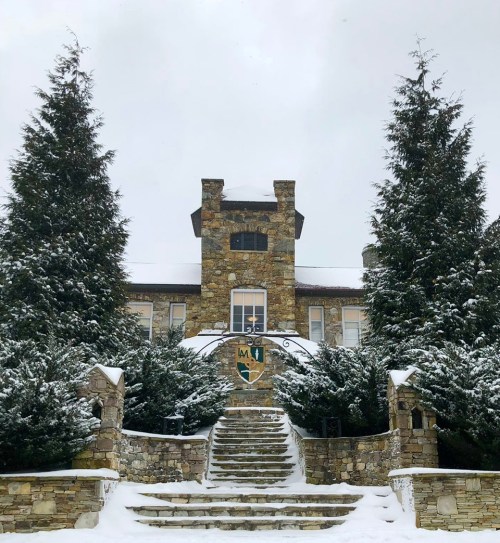 A stone building with a tower, surrounded by snow-covered trees and a staircase leading to the entrance.