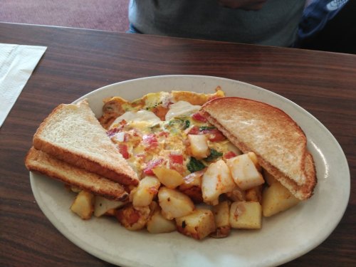 A plate of breakfast featuring an omelet with vegetables, diced potatoes, and two slices of toasted bread.