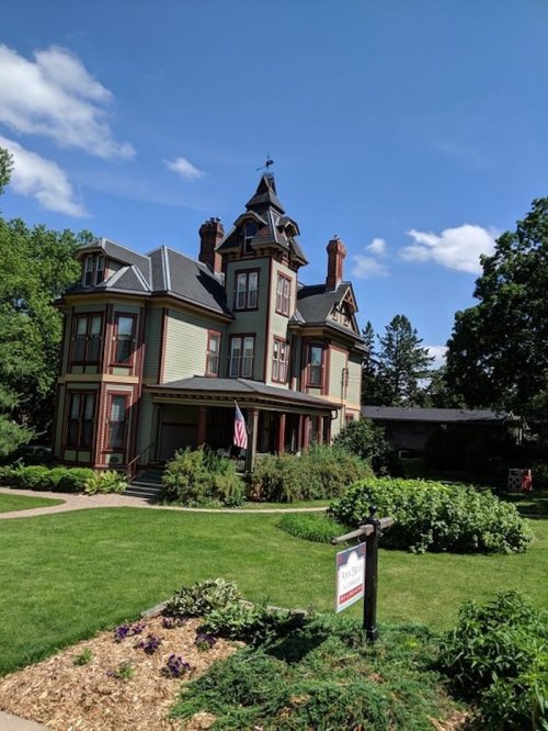 A large, ornate Victorian house with a tower, surrounded by lush greenery and a clear blue sky.