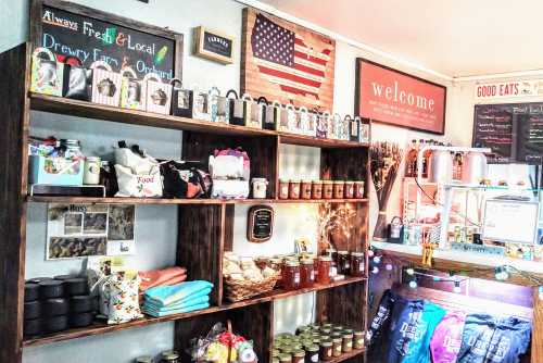 A cozy shop interior with shelves displaying local products, jars, and snacks, featuring an American flag and welcoming signs.