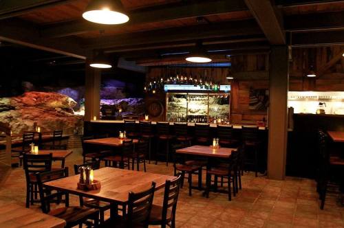 Cozy restaurant interior with wooden tables, chairs, and a bar, featuring soft lighting and stone accents.