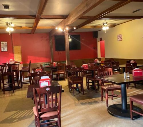 Empty restaurant interior with wooden tables and chairs, red walls, and ceiling fans.