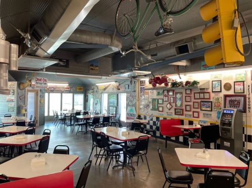 A retro diner interior with red and black tables, vintage decor, and a bicycle hanging from the ceiling.