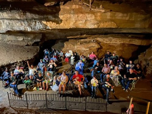 A large group of people seated in folding chairs inside a cave, enjoying an event in a natural rock setting.