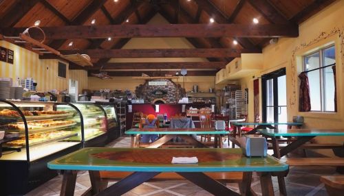 Cozy restaurant interior with wooden beams, colorful tables, a display case of pastries, and a warm, inviting atmosphere.