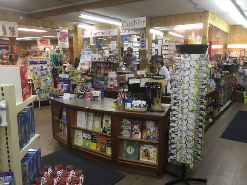 A busy store interior featuring a cashier area, shelves of products, and a display rack of cards and gifts.