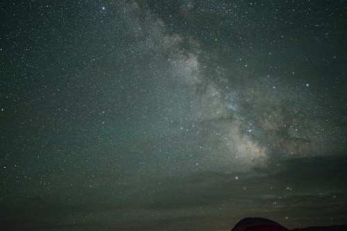 A starry night sky featuring the Milky Way, with scattered stars and a hint of clouds.