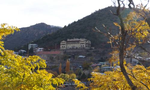A hillside view of a large building surrounded by trees and mountains, with autumn foliage in the foreground.