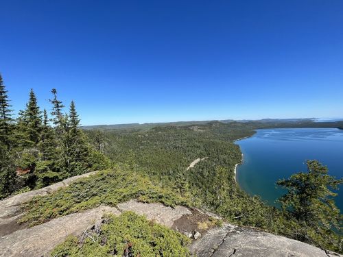 A panoramic view of a lush green landscape meeting a calm blue lake under a clear blue sky.