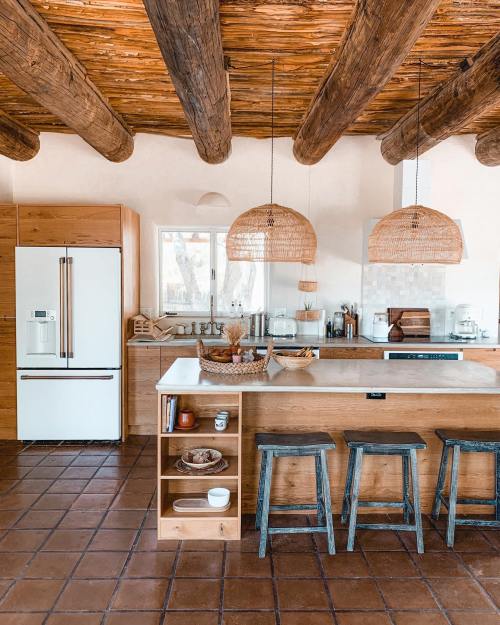 A modern kitchen with wooden beams, a large island, woven pendant lights, and natural materials throughout.