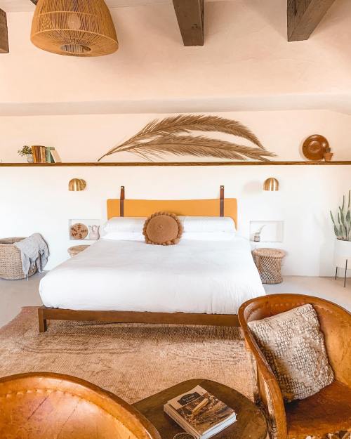Cozy bedroom with a white bed, decorative pillows, woven chairs, and natural elements in a warm, inviting atmosphere.