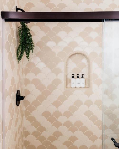 A modern shower with a scalloped tile wall, a glass door, and a niche holding three bottles of shampoo.
