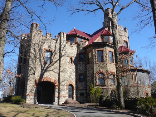 A large stone castle with turrets and a red roof, surrounded by trees and a clear blue sky.