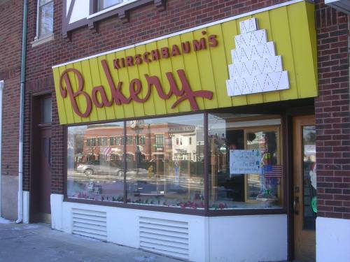 A bakery storefront with a yellow sign reading "Kirschbaum's Bakery" and a decorative cake display in the window.