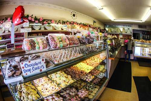 A colorful bakery display filled with various cookies and pastries, with a cozy interior and floral decorations.