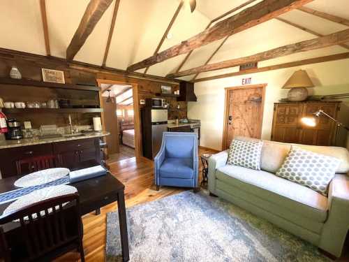 Cozy cabin interior featuring a living area with a sofa, chair, dining table, and kitchenette with wooden beams.