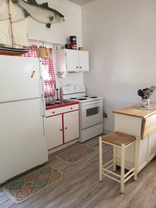 A cozy kitchen with white cabinets, a red-accented stove, and a wooden island, featuring nautical decor and patterned rugs.