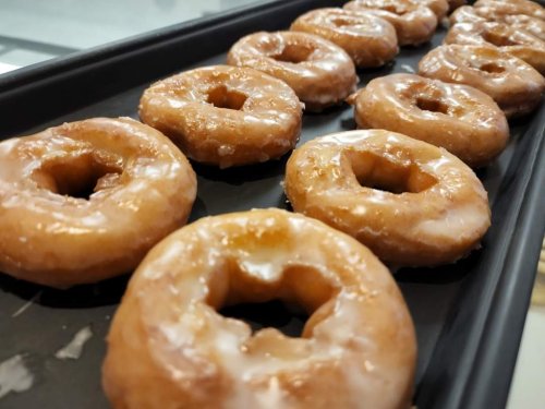 A tray of freshly glazed donuts arranged in a row, glistening with a sweet, shiny coating.