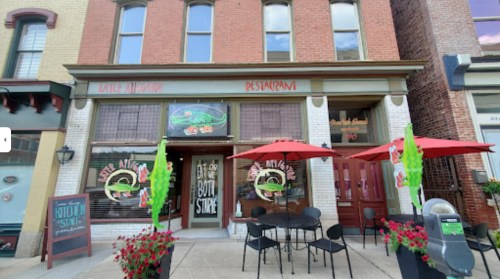A restaurant with a colorful facade, outdoor seating, and a sign for a bottle store. Bright umbrellas and decorations are visible.