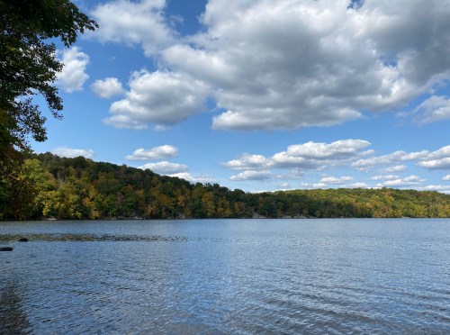 A serene lake surrounded by trees with autumn foliage under a partly cloudy sky.