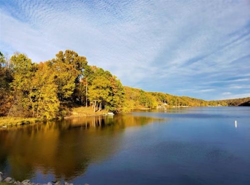A serene lake surrounded by autumn trees, reflecting the colorful foliage and a cloudy sky.