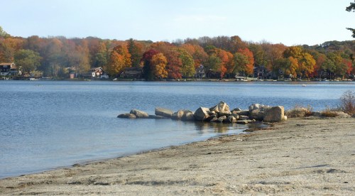 A serene lake scene with colorful autumn trees and rocky shoreline under a clear sky.