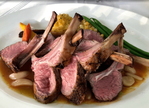 A plate of grilled lamb chops served with green beans, corn, and colorful vegetables in a savory sauce.