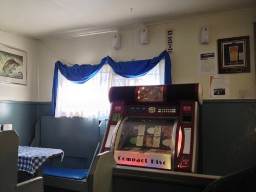 A cozy diner interior featuring a jukebox, blue curtains, and a checkered tablecloth.