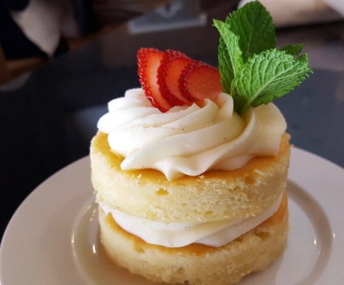 A layered cake with cream frosting, topped with sliced strawberries and a mint leaf, served on a white plate.