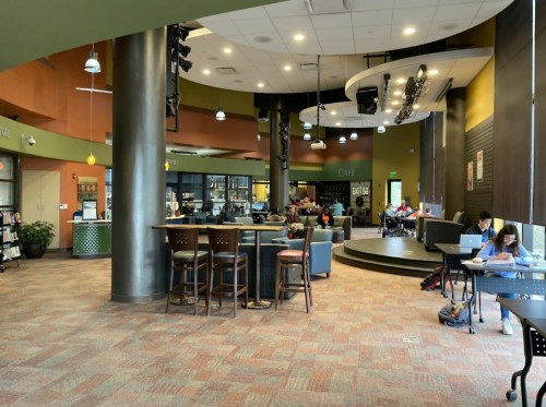 A cozy café space with seating, tables, and people working or studying in a vibrant, modern environment.