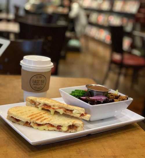 A toasted sandwich with cheese and bacon, a side salad, and a coffee cup on a wooden table in a café setting.