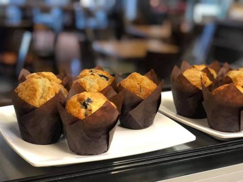 A plate of freshly baked muffins in dark paper liners, displayed in a cozy café setting.